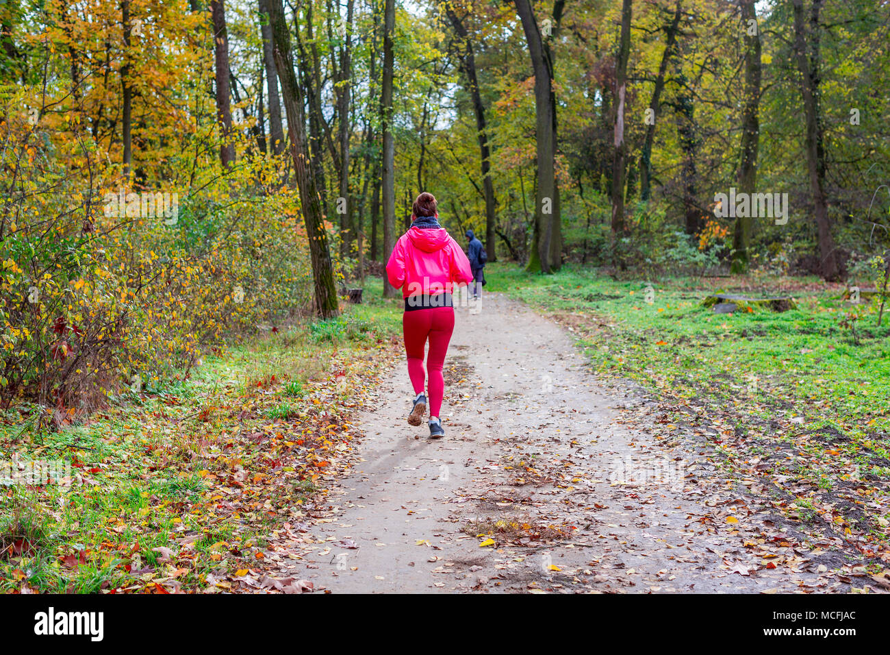 Young sporty woman in pink sport suit running in the autumn forest. Back view with space for text. Healthy lifestyle concept Stock Photo