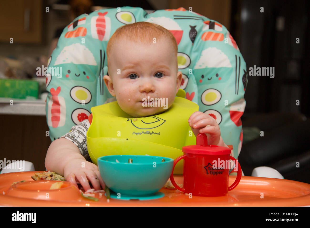 12 month old red haired baby boy in a highchair eating Stock Photo