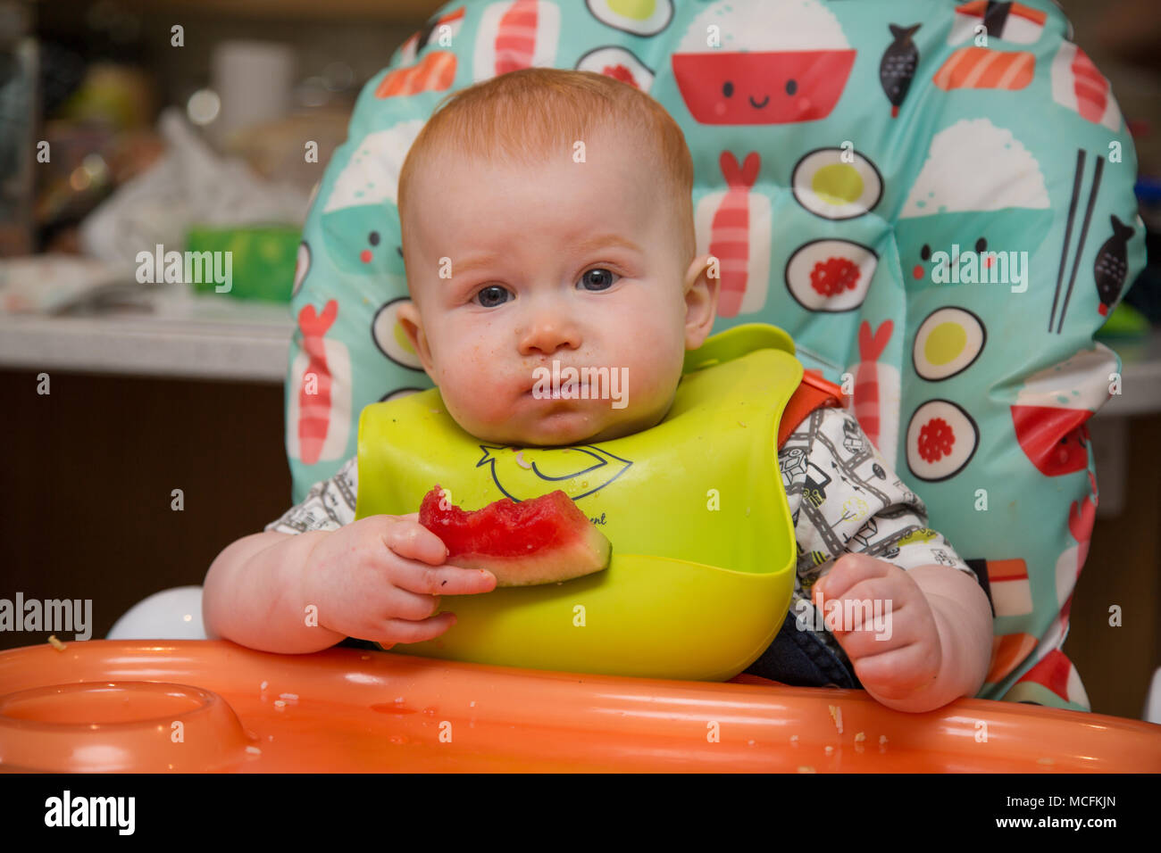 12 month old red haired baby boy in a highchair eating Stock Photo