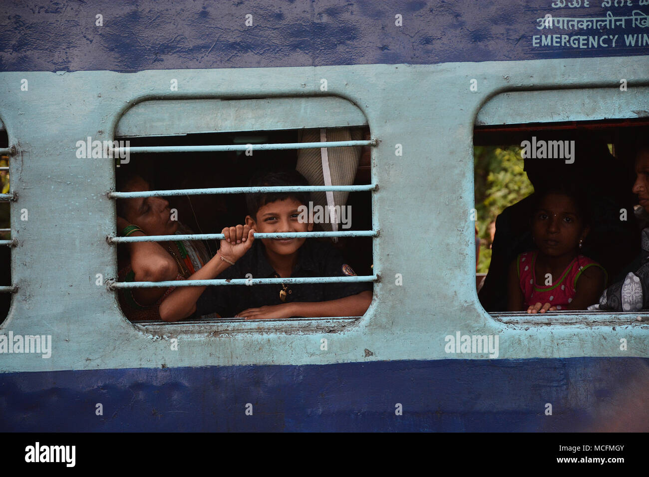 Family travelling on a train in India and the boy peering out of the barred window from the carriage Stock Photo