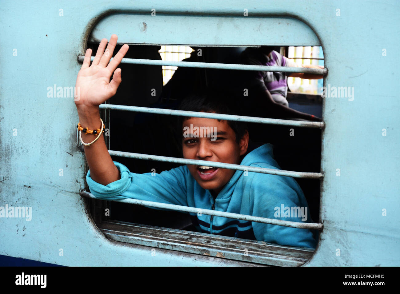 A very friendly young boy waving from the carriage of a train in India Stock Photo