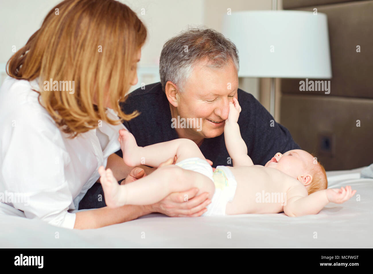 Grandparents and the baby are playing on the bed in the bedroom Stock