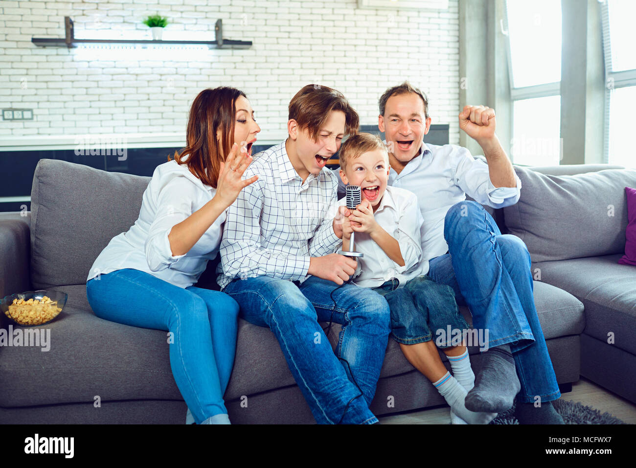 A happy family sings karaoke songs into the microphone in the room. Stock Photo