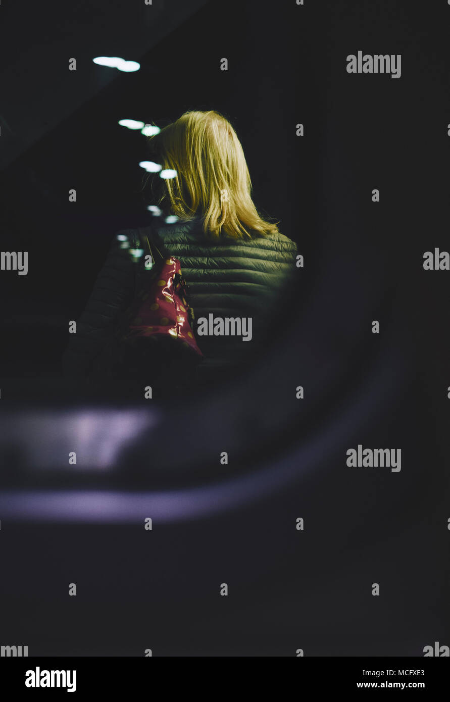 A lone girl with blonde hair standing outside a window at night. Stock Photo