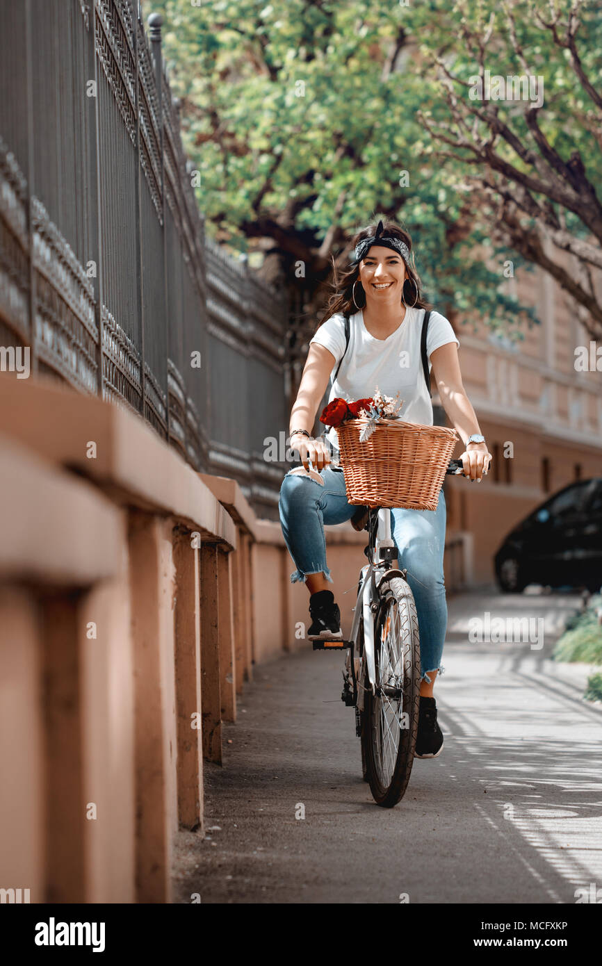 Happy woman riding the bike along the city street, in summer sunny day, smiling of joy during outdoor activity. Stock Photo