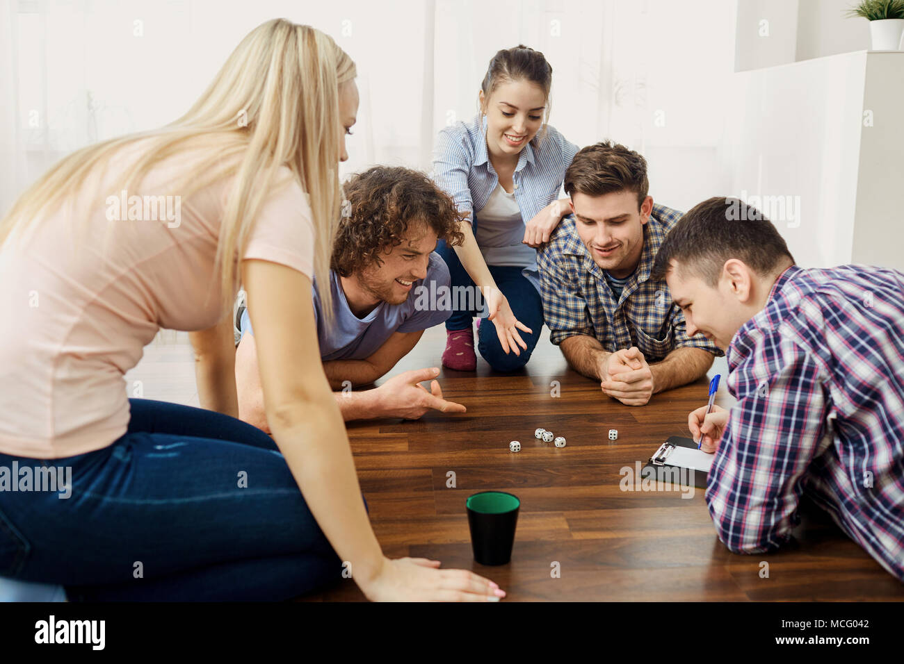 A group of friends play board games on the floor having fun at a party indoors. Stock Photo