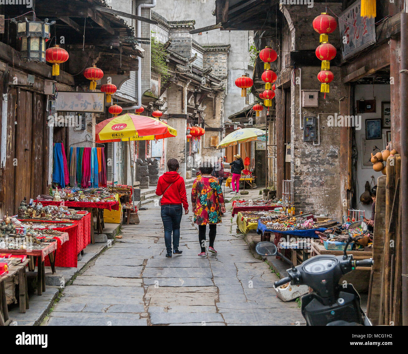 Chinese tourists wander among the shops and stalls of Daxu market. Cheap trinkets, mementos and jewellery line the street. Daxu, China. Stock Photo