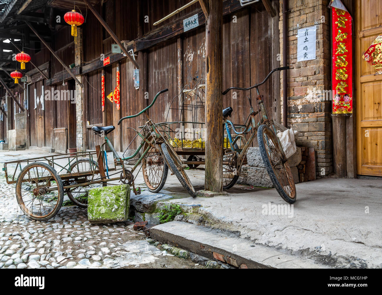 Two tricycles parked by a doorway on a cobbled street in the ancient town of Daxu, China. Red Chinese lanterns hang from canopies and line the street. Stock Photo