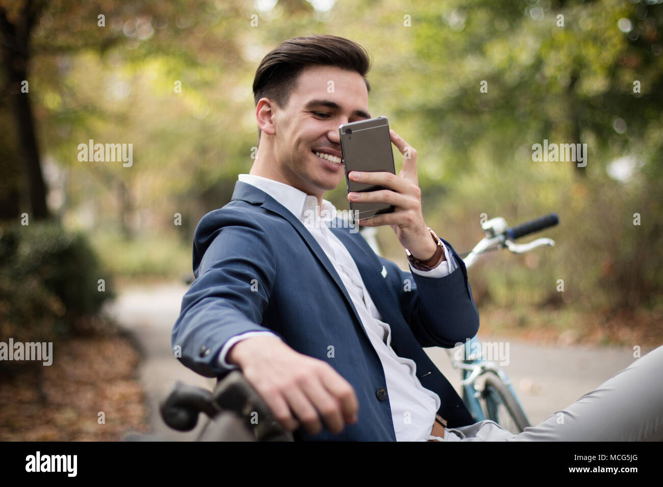 Young attractive and happy businessman taking a picture with his smartphone outdoors in the park. Stock Photo