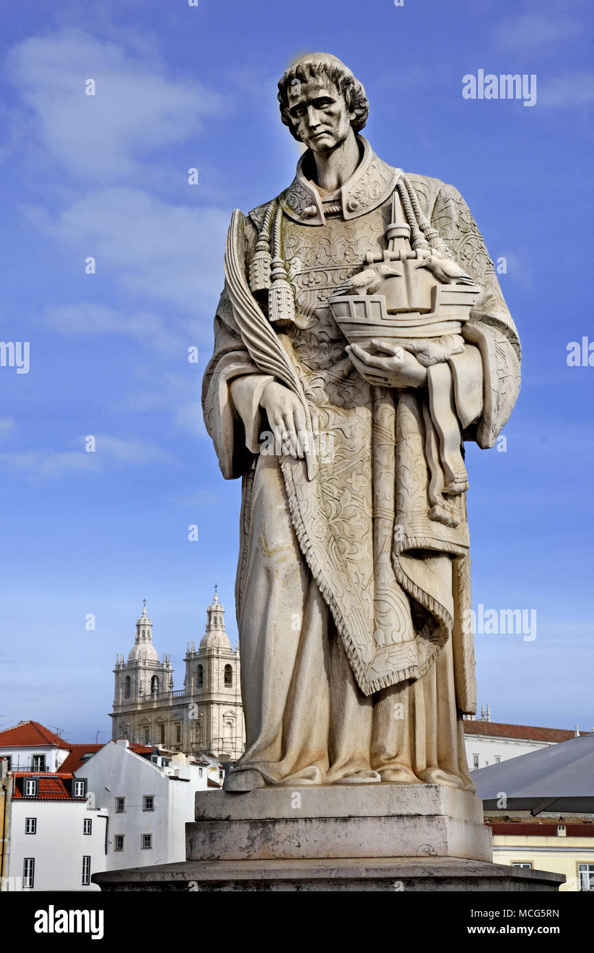Martyr São Vicente, patron Saint of Lisbon. He holds a ship with two ravens, the city's emblem.  Marble statue on the terrace of Largo das Portas do Sol Alfama, Lisbon - Lisboa, Portugal  Portuguese. ( Saint Vincent statue Fora monastery in the background ) Stock Photo