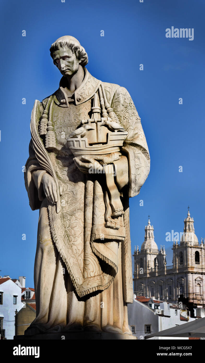 Martyr São Vicente, patron Saint of Lisbon. He holds a ship with two ravens, the city's emblem.  Marble statue on the terrace of Largo das Portas do Sol Alfama, Lisbon - Lisboa, Portugal  Portuguese. ( Saint Vincent statue Fora monastery in the background ) Stock Photo