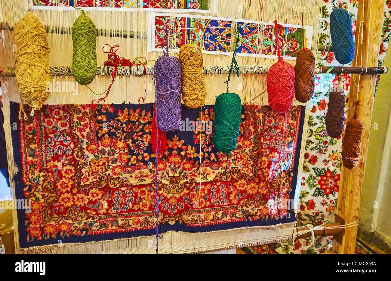 Hand weaving loom with examples of colored woolen yarns and traditional Persian carpet, covered