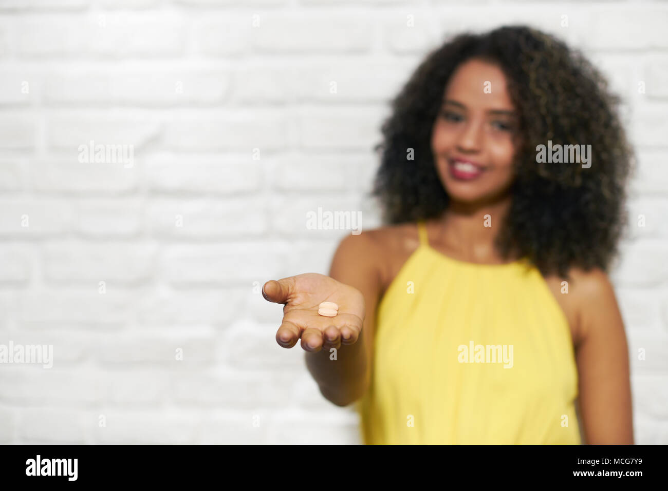 Young Black Woman On Brick Wall Taking Vitamin Pills Stock Photo