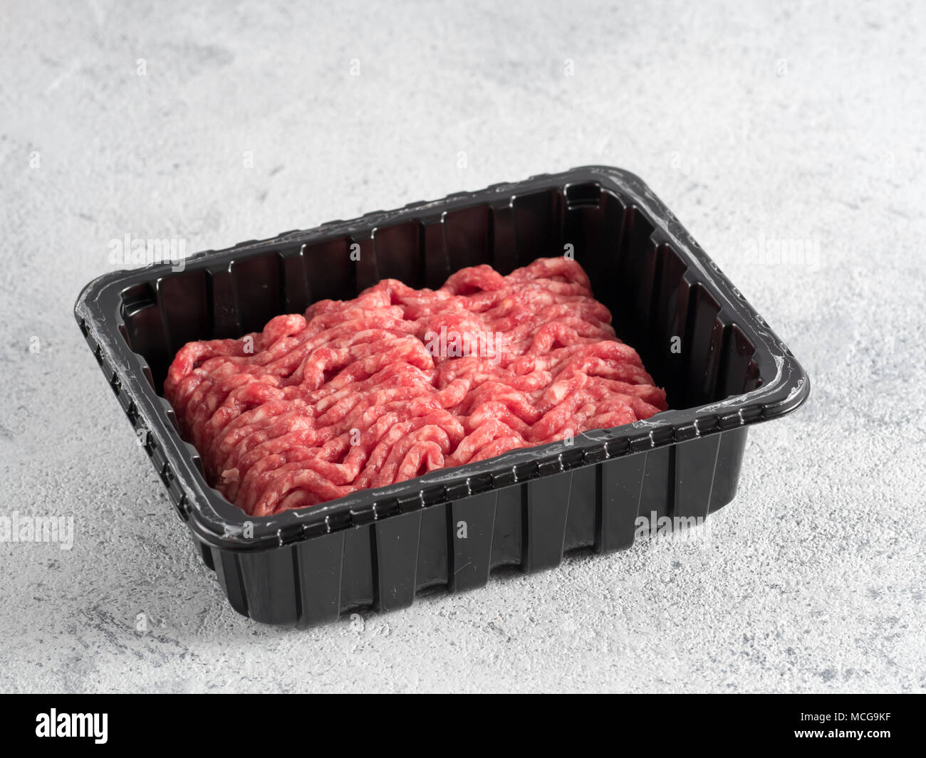 Fresh raw minced beef in plastic tray over light gray cement background