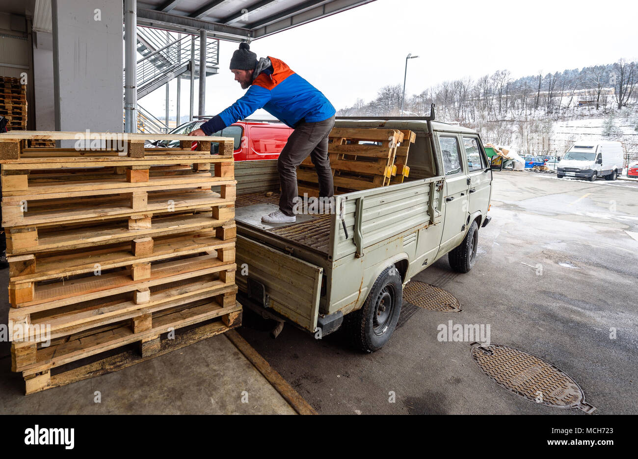 Man is loading wooden pallets on a truck in winter. Stacking wooden