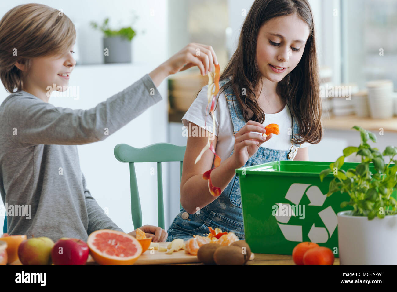 Girl and boy trowing out fruits waste into green recycling container Stock Photo