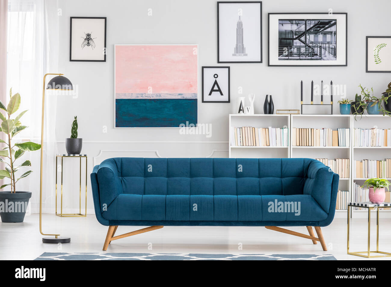 Comfy, blue couch set in white living room interior with bookshelf and paintings Stock Photo