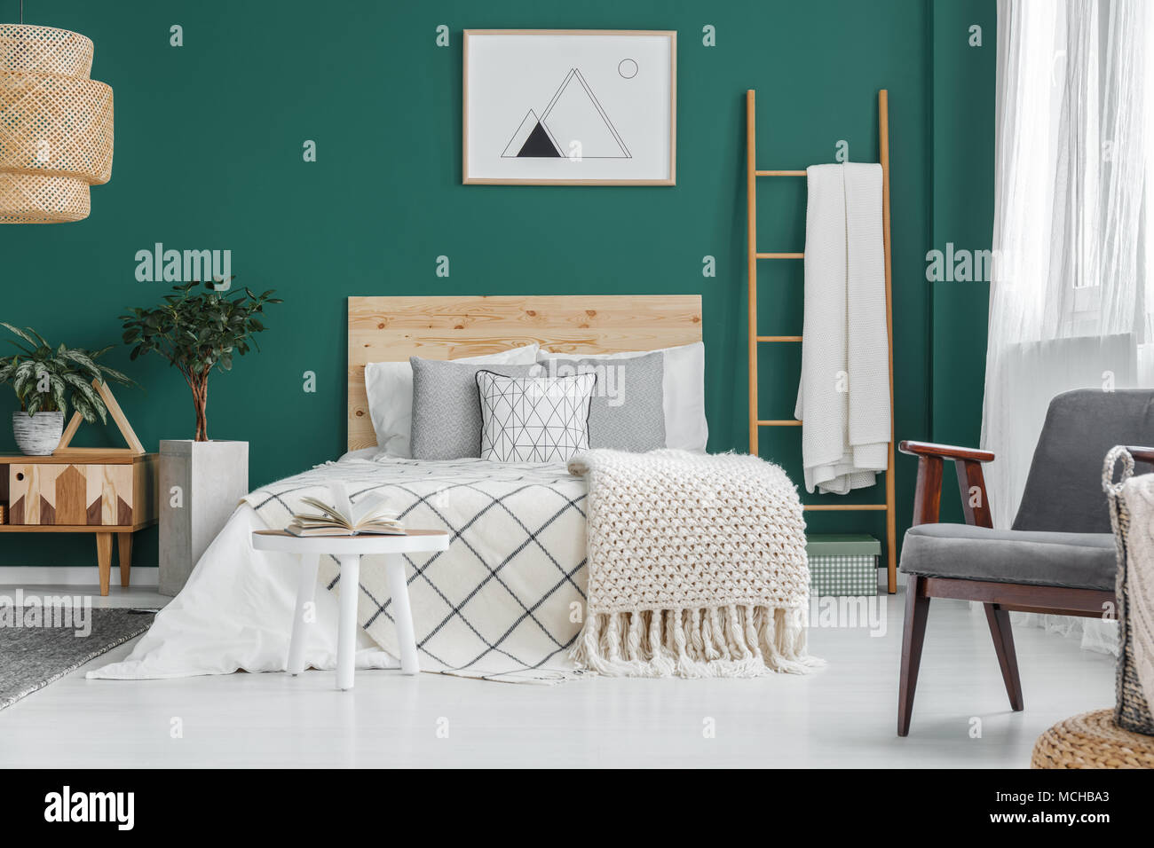 Poster on green wall above bed in bedroom interior with grey armchair and  ladder Stock Photo - Alamy
