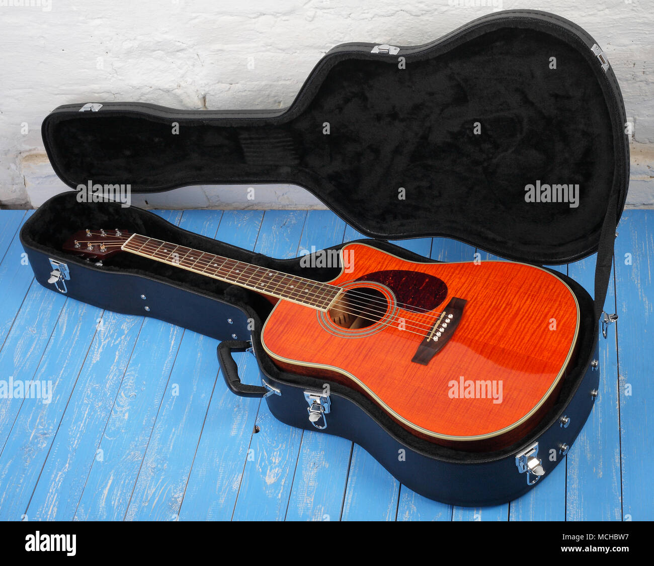 Musical instrument - Orange acoustic guitar in hard case on a blue wood, and white brock wall background. Stock Photo