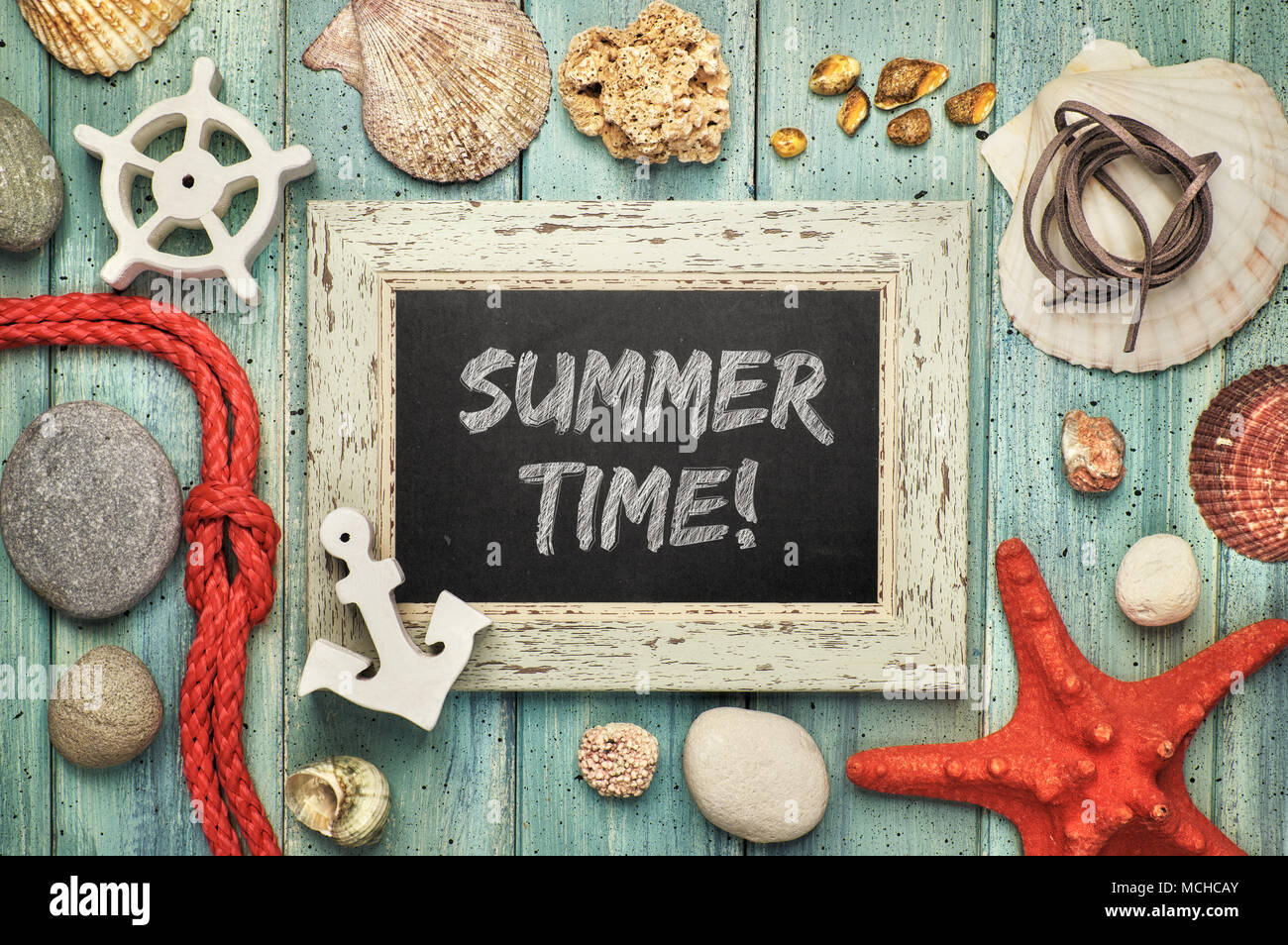 Blackboard with 'Summer time' chalk text, with sea shells, rope and star fish on light green wooden background Stock Photo