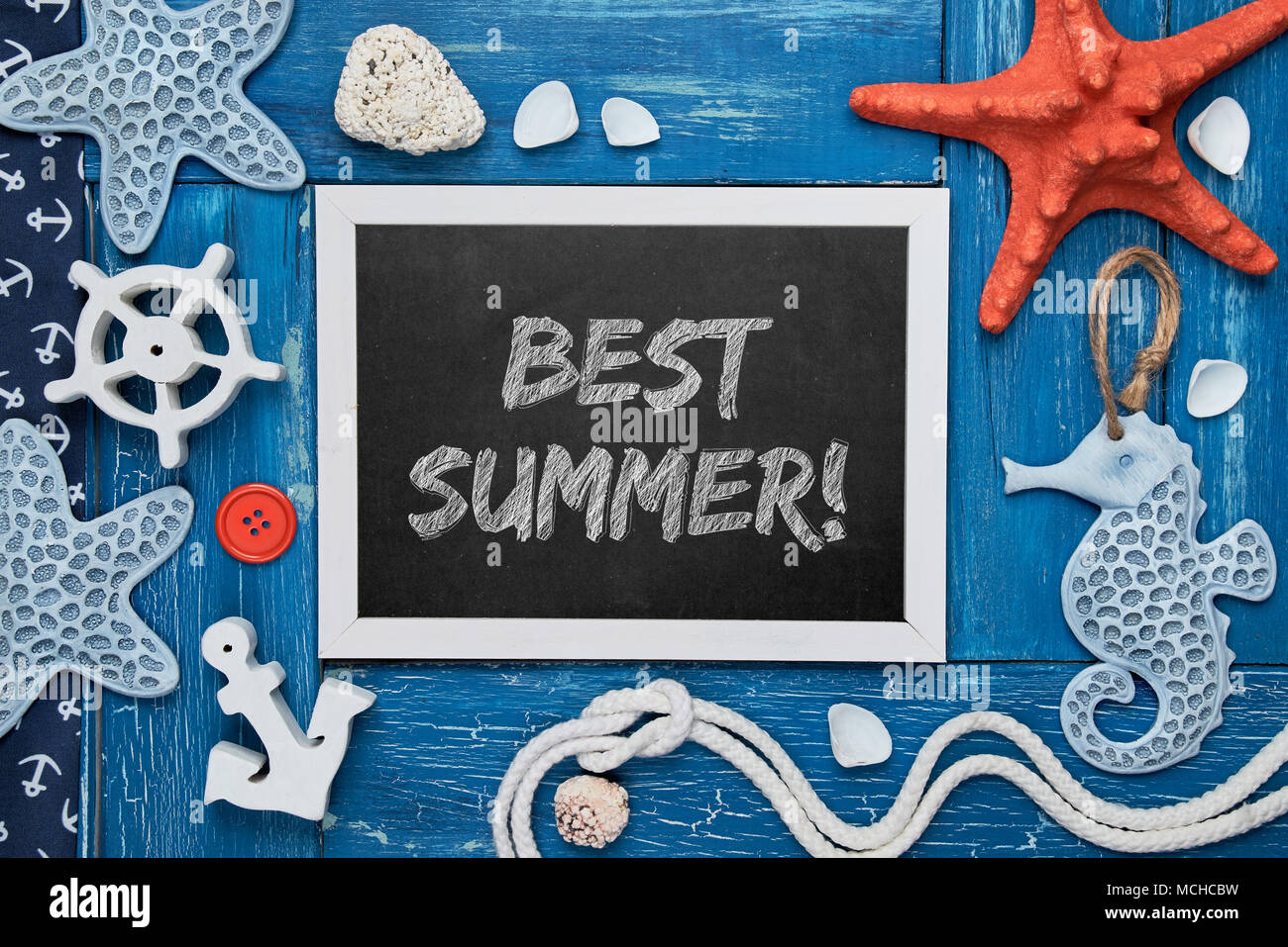 Blackboard with 'Hello Summer!' chalk text, with sea shells, rope and star fish on blue wooden background Stock Photo
