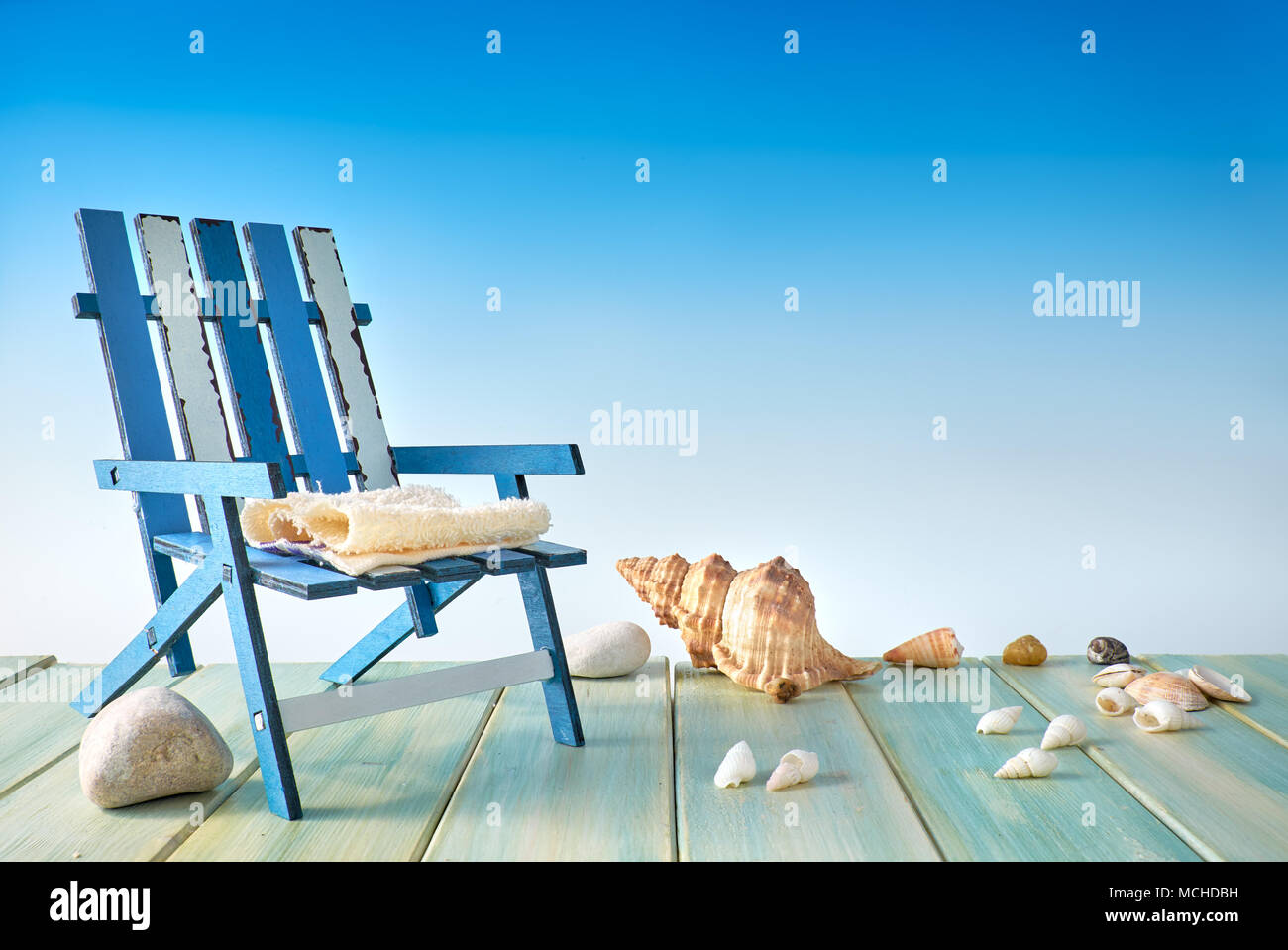 Summertime holiday background with text space. Beach chair on wooden terrace with sea shells, seaside decorations, copy-space on blue background. Stock Photo