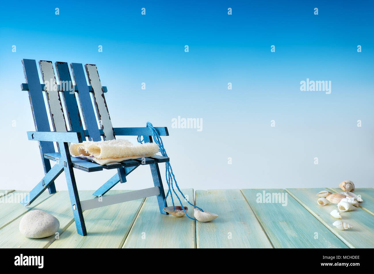Summertime holiday background with text space. Beach chair on wooden terrace with sea shells, seaside decorations, copy-space on blue background. Stock Photo