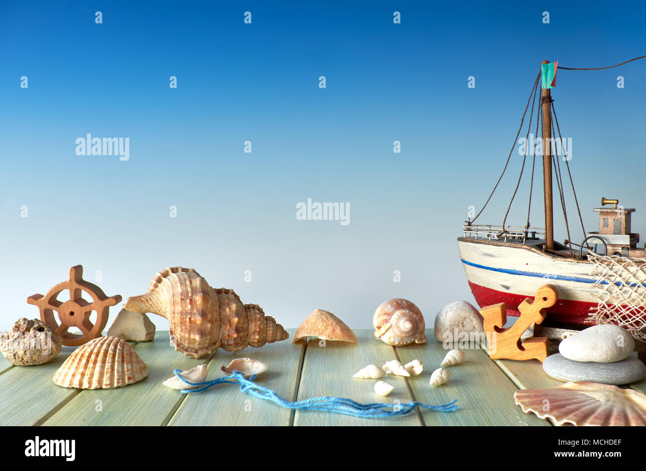 Summertime decorations: sea shells, wooden ship, anchor and stoned on blue gradient background, text space Stock Photo