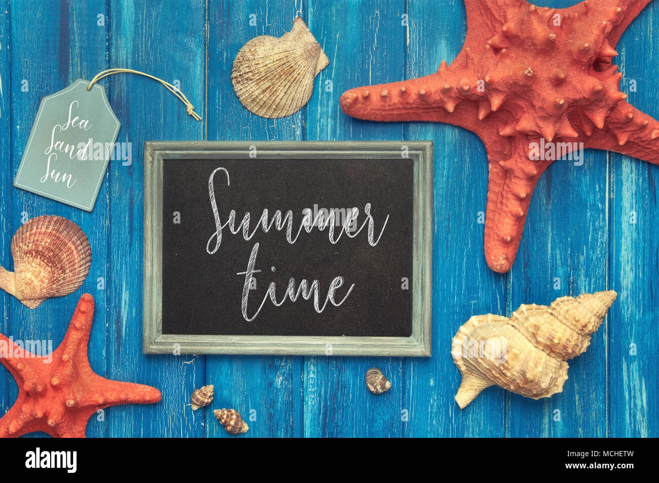 Blackboard with 'Summer time' chalk text, with sea shells, rope and star fish on blue  wooden background Stock Photo