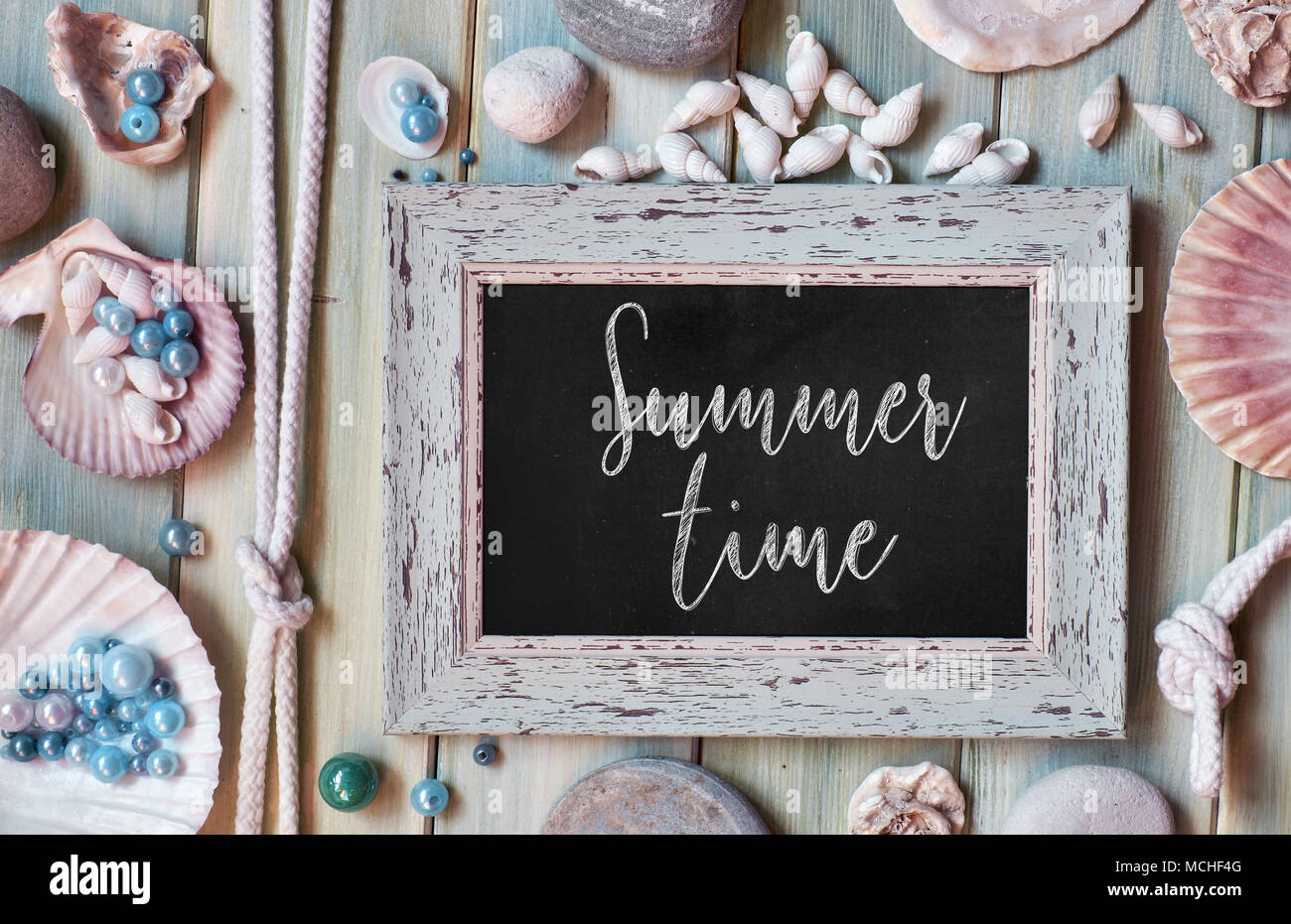 Blackboard with 'Summer time' chalk text, with sea shells, rope and star fish on light wooden background Stock Photo