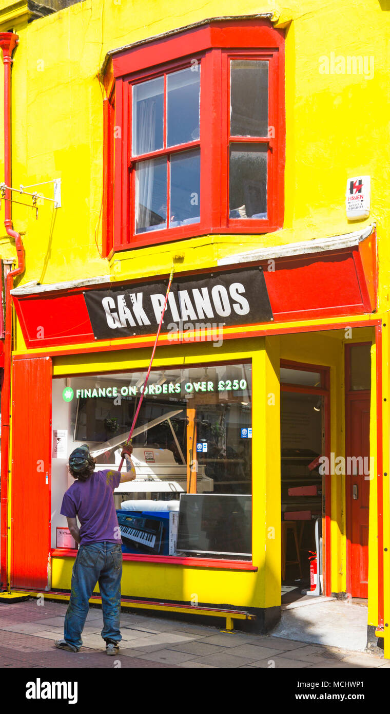 Man painting yellow walls on frontage of GAK Pianos Piano Showroom in North Road, Brighton, East Sussex, England UK in April Stock Photo