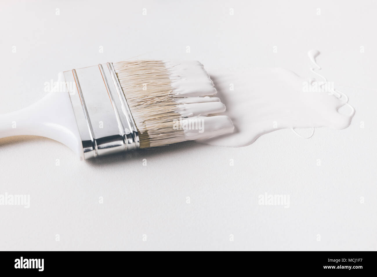 one paint brush in white paint on surface isolated on white Stock Photo