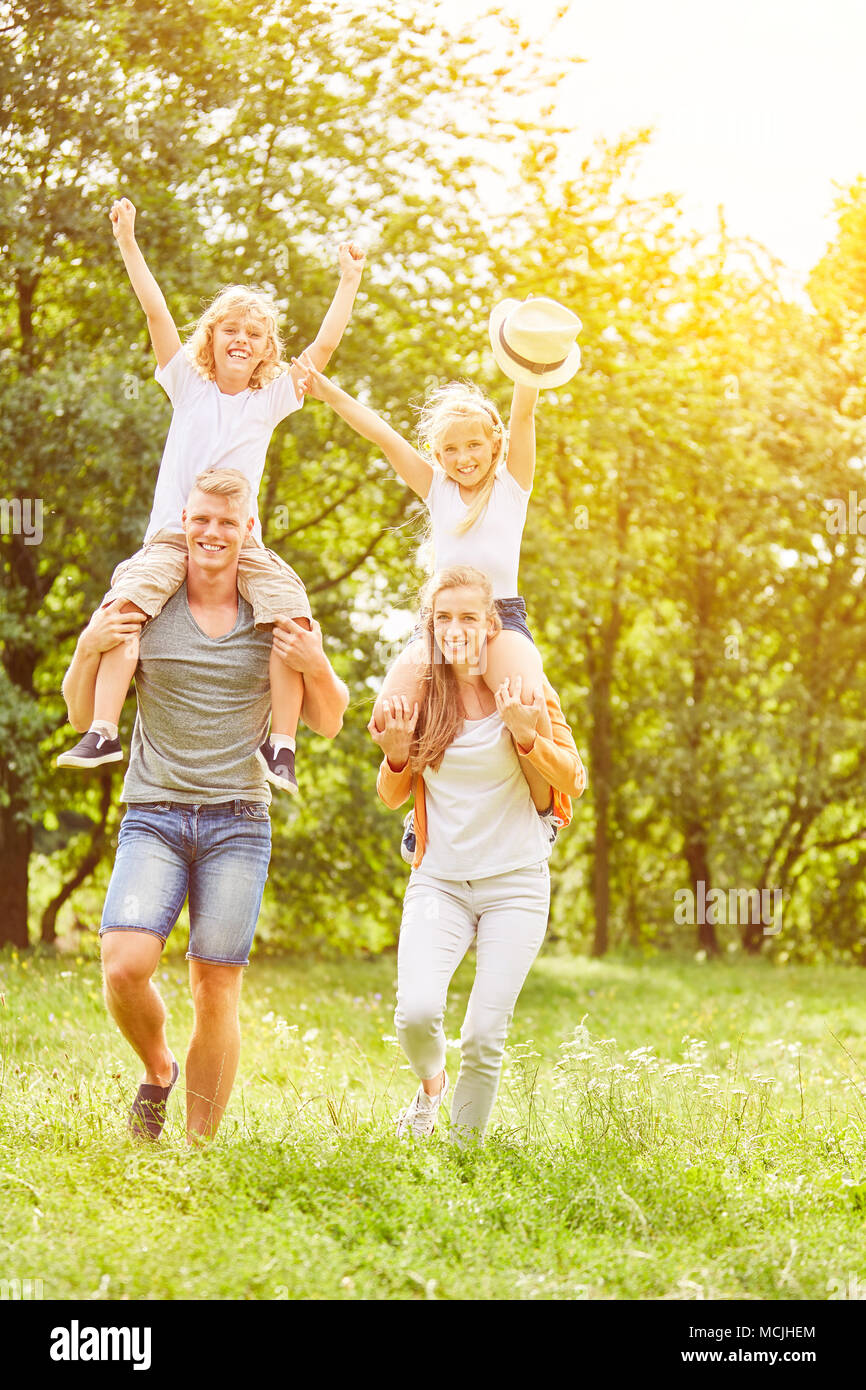 Two laughing parents carry their children piggyback in summer on a meadow Stock Photo