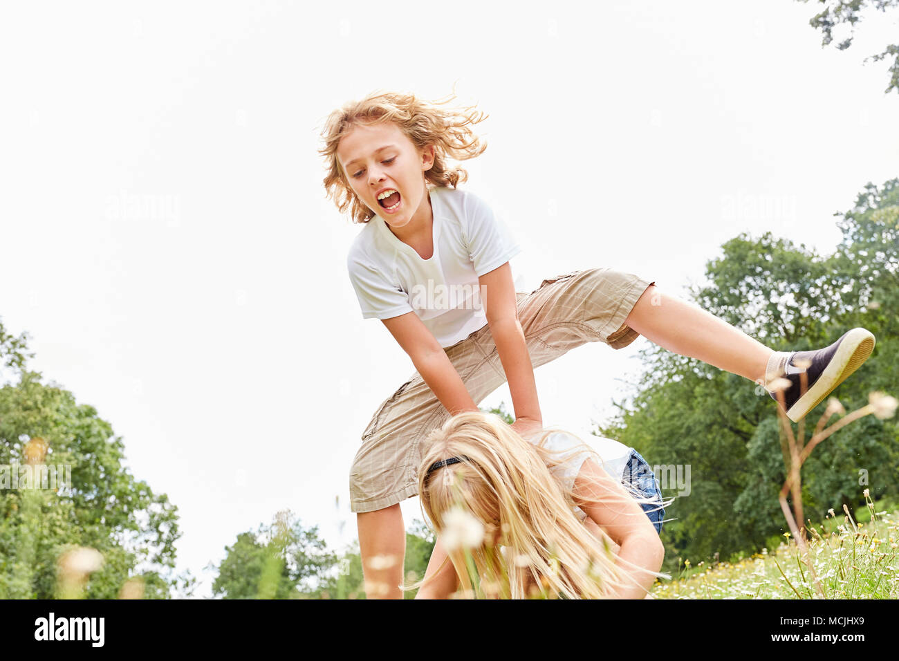 Children make leapfrog on a meadow in the summer vacation Stock Photo