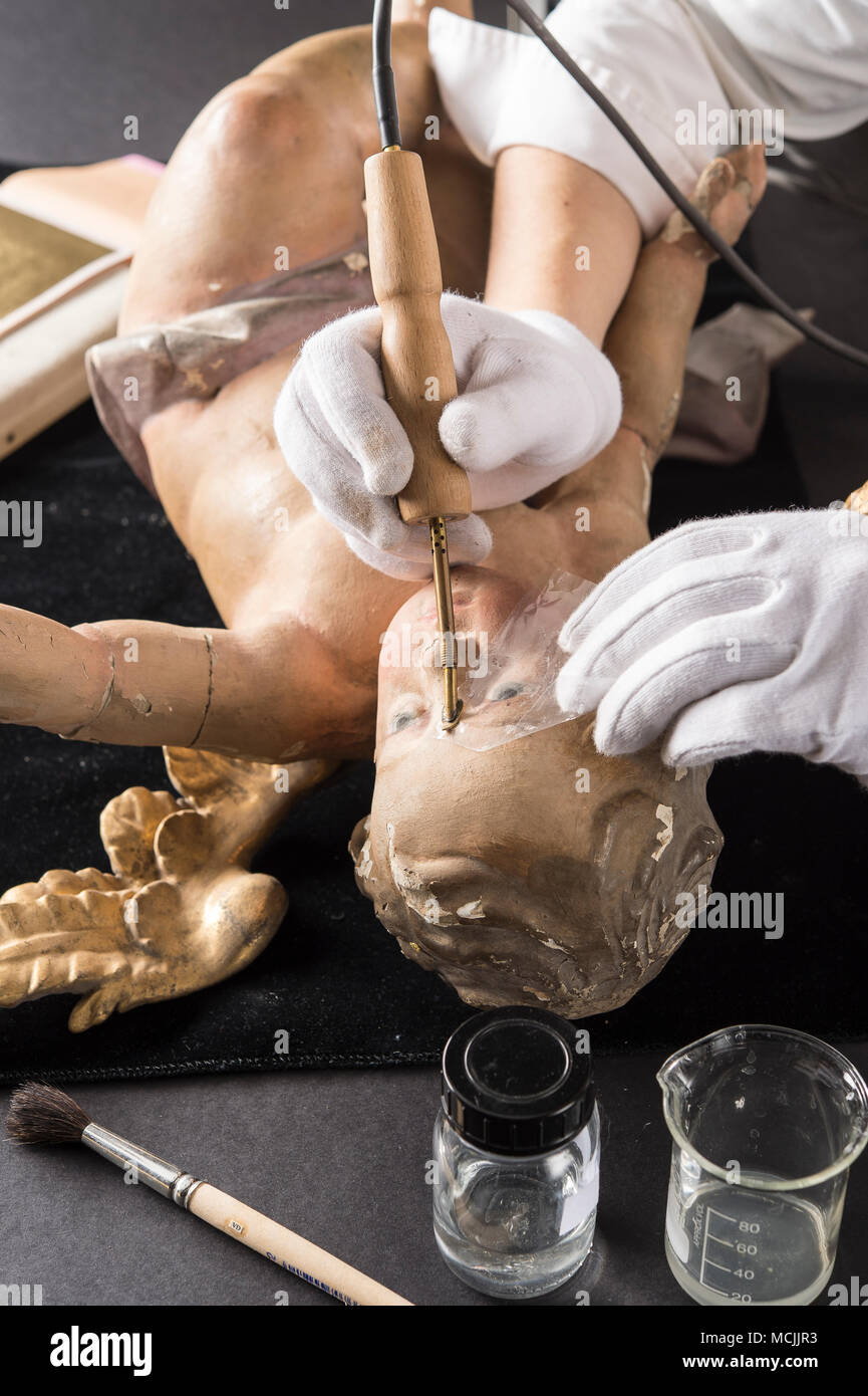 Restoration studio, restorer, hands smoothing glue with heating spatula on angel's face, for fixing the filling material, Munich Stock Photo