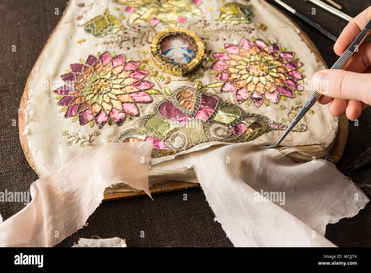 Restoration studio, restorer, hand holds fabric samples with tweezers on torn, artfully embroidered silk cloth, Munich, Bavaria Stock Photo