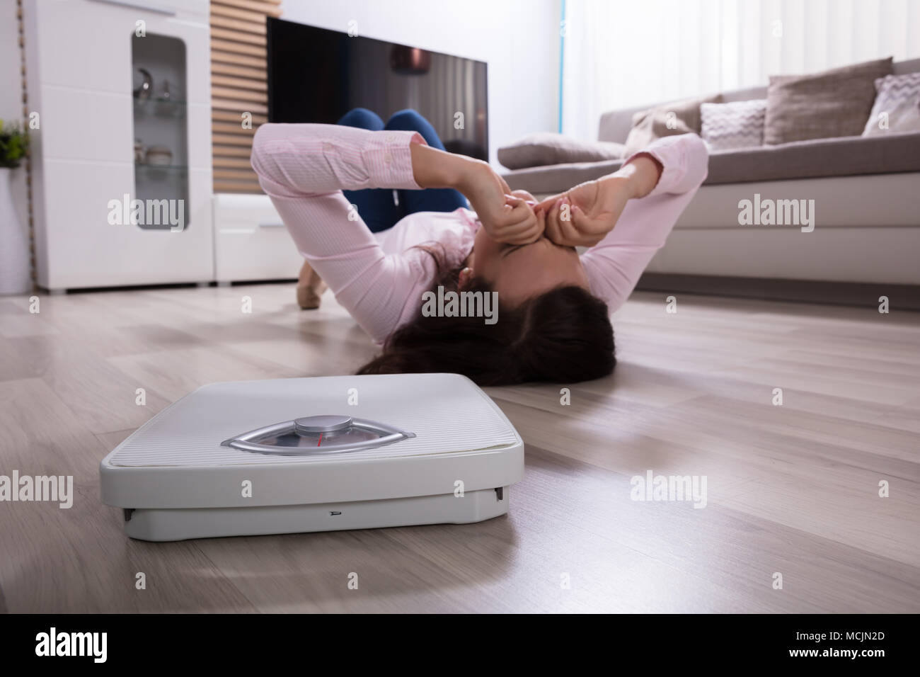 Close-up Of A Weighing Scale Besides Woman Lying On Hardwood Floor Stock Photo