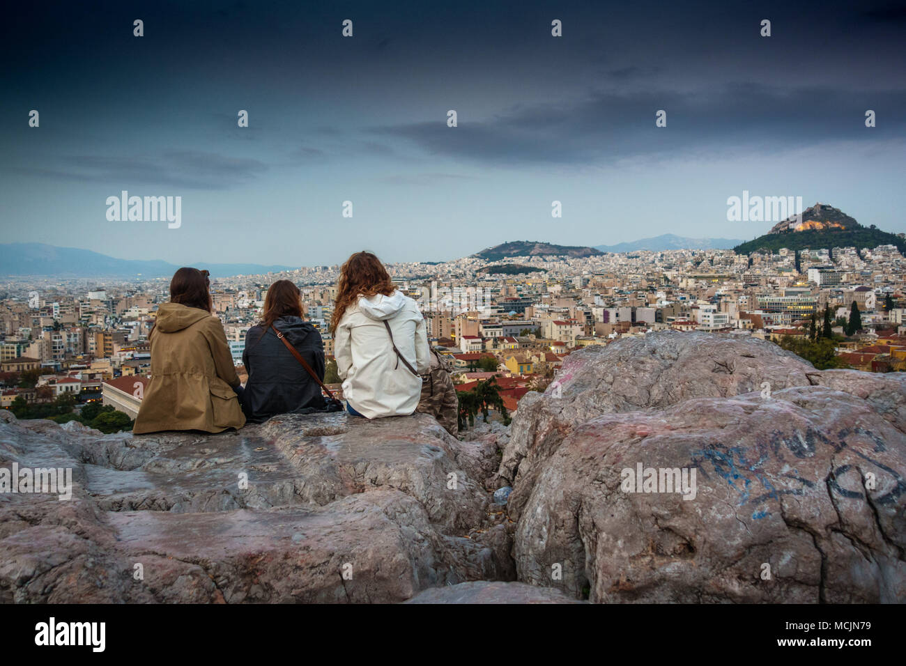 Three young women sitting on boulders and sightseeing Athens city, Greece Stock Photo
