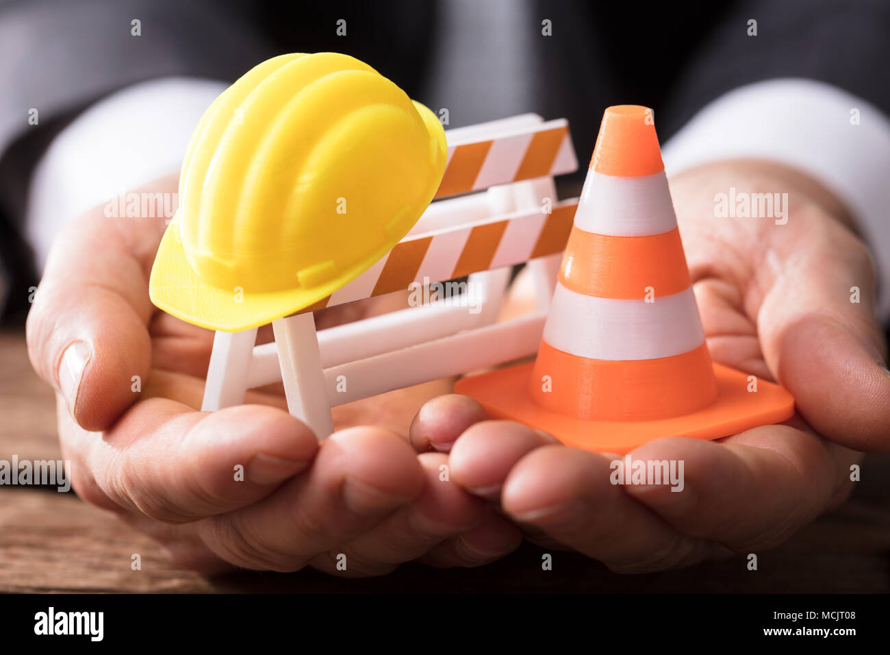 Close-up Of Human Hand Holding Barricade With Traffic Cone And Hard Hat Stock Photo
