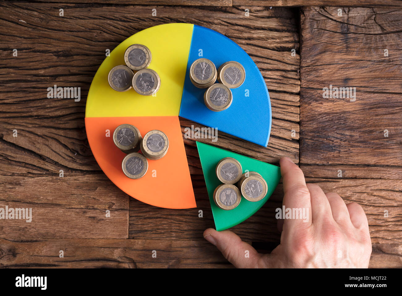High Angle View Of Businessperson's Hand Taking Piece With Money From Pie Chart Stock Photo