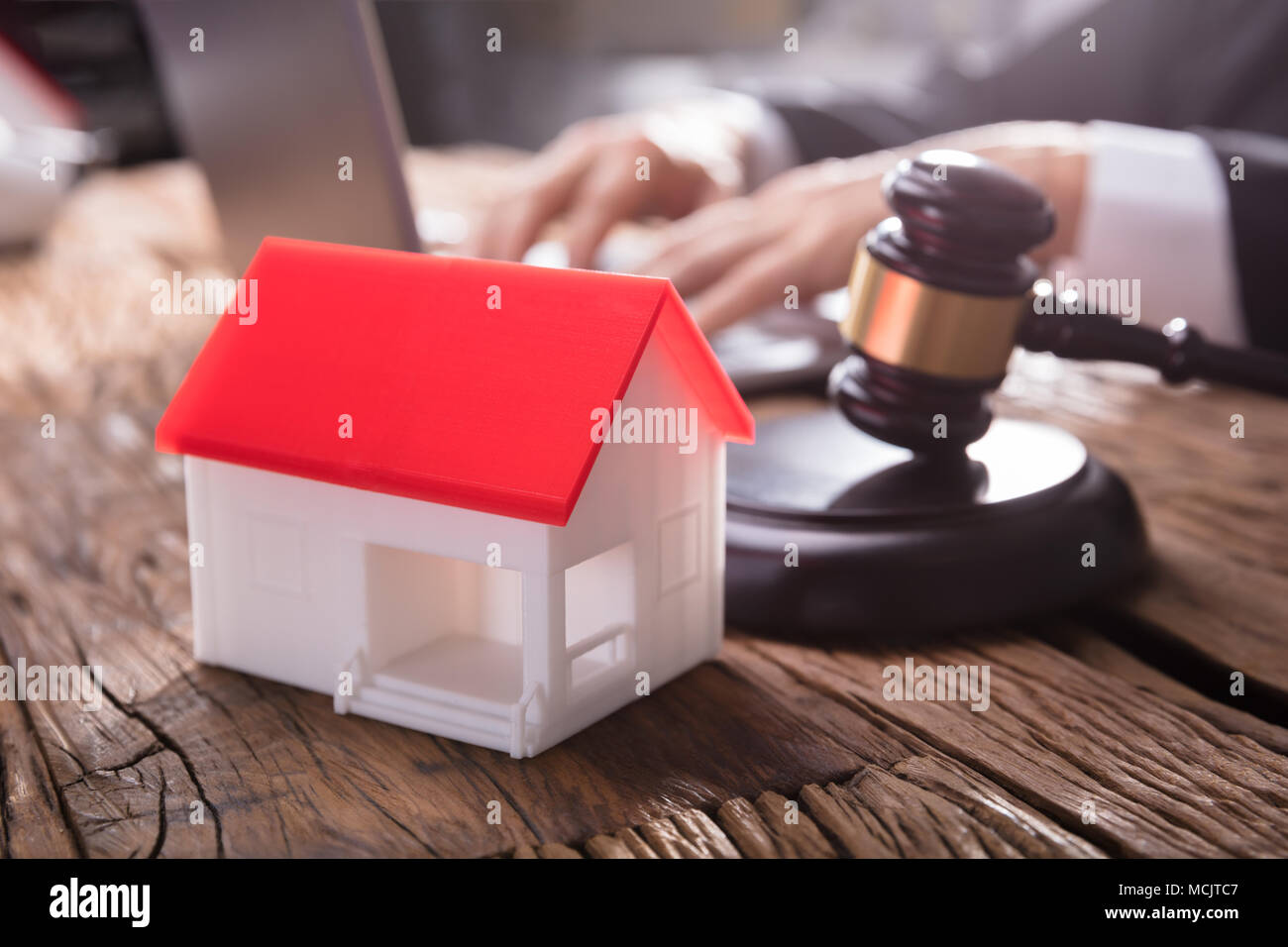 Close-up Of House Model With Red Roof And Gavel On Wooden Desk In Courtroom Stock Photo