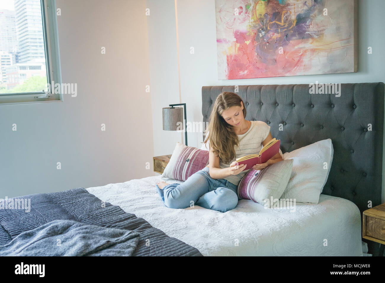 Relaxed young woman reading book in bed at home Stock Photo