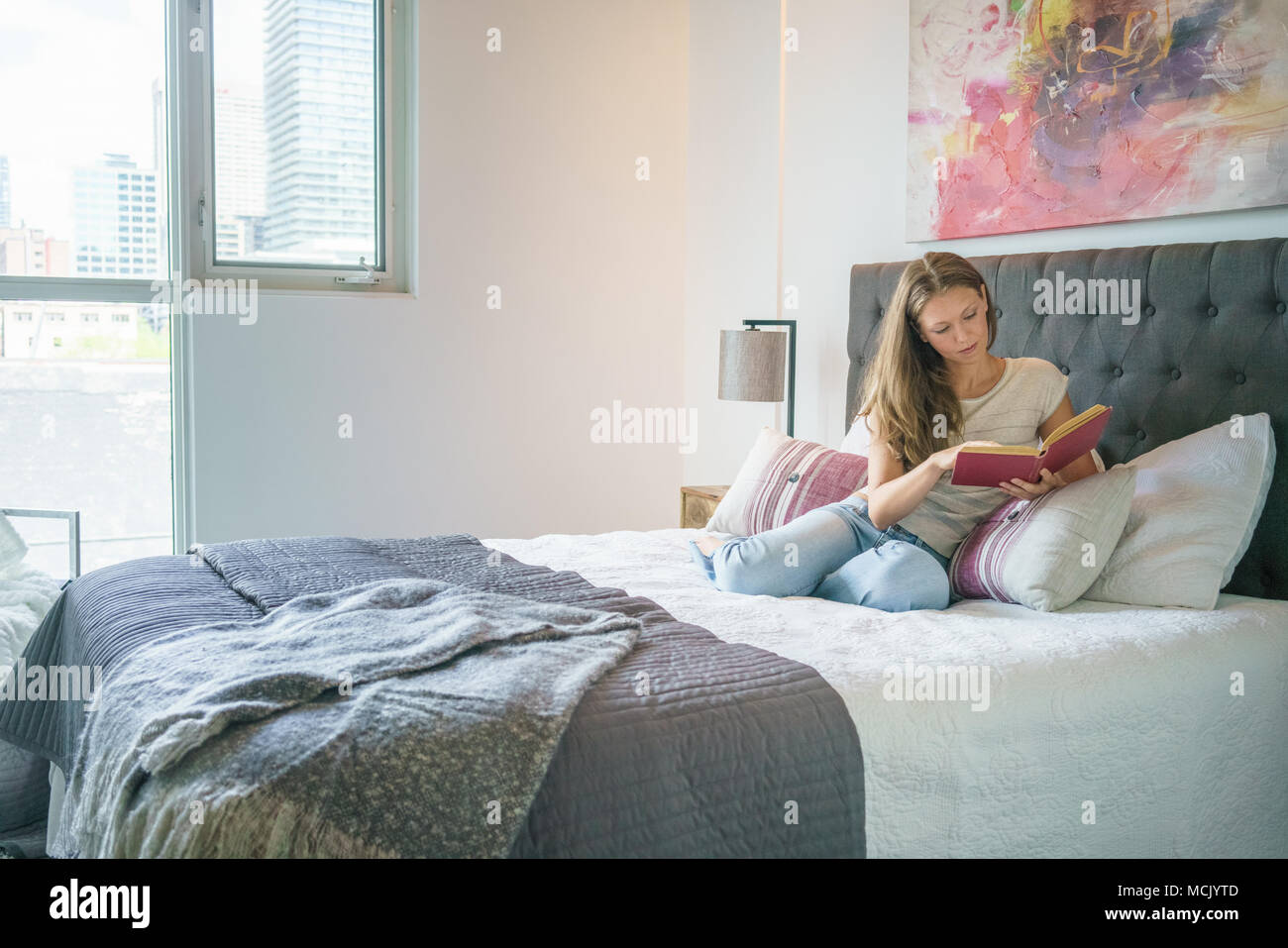 Relaxed young woman reading book in bed at home Stock Photo