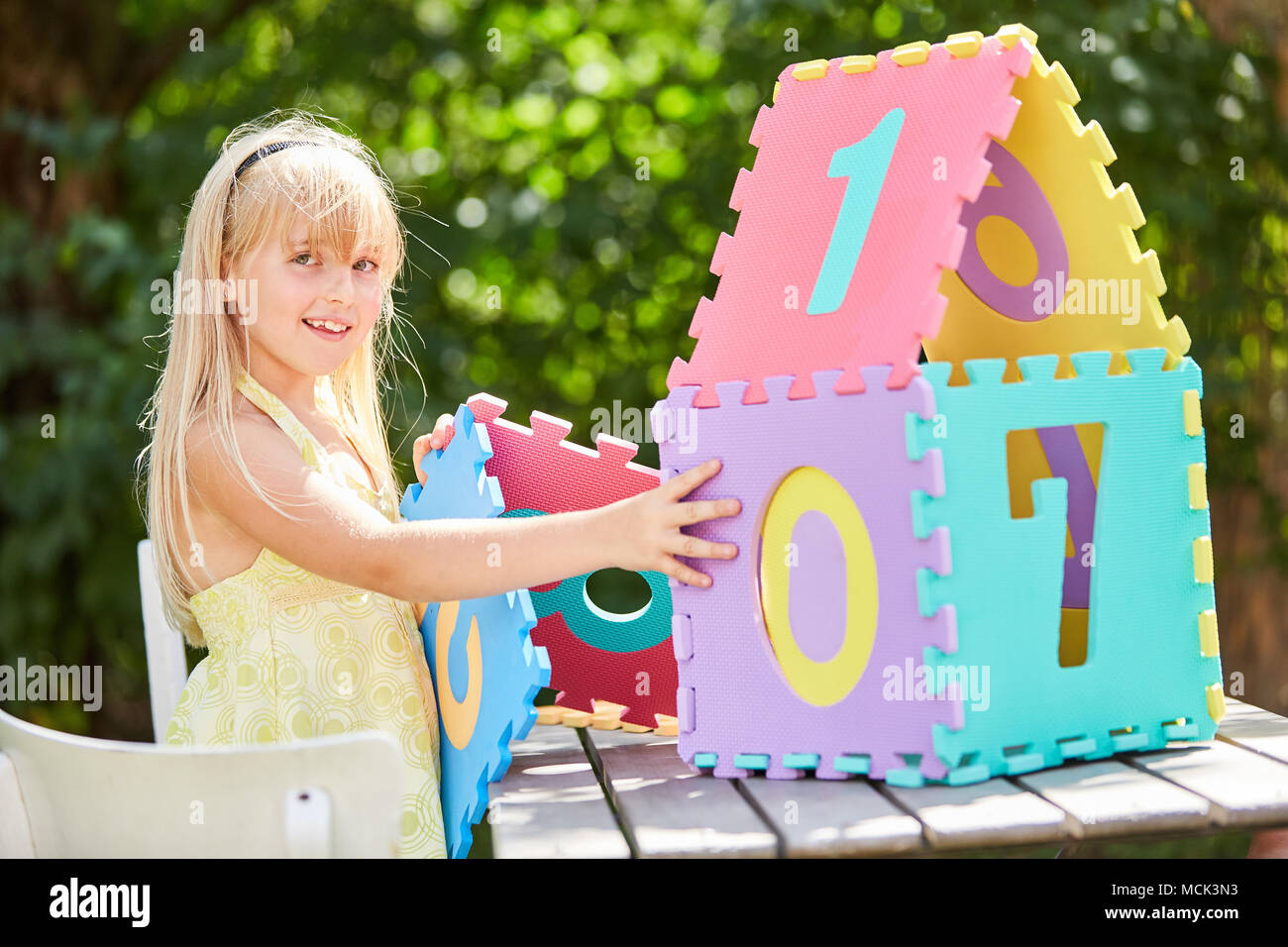 Blonde girl builds a miniature house out of puzzle pieces as a dream house Stock Photo