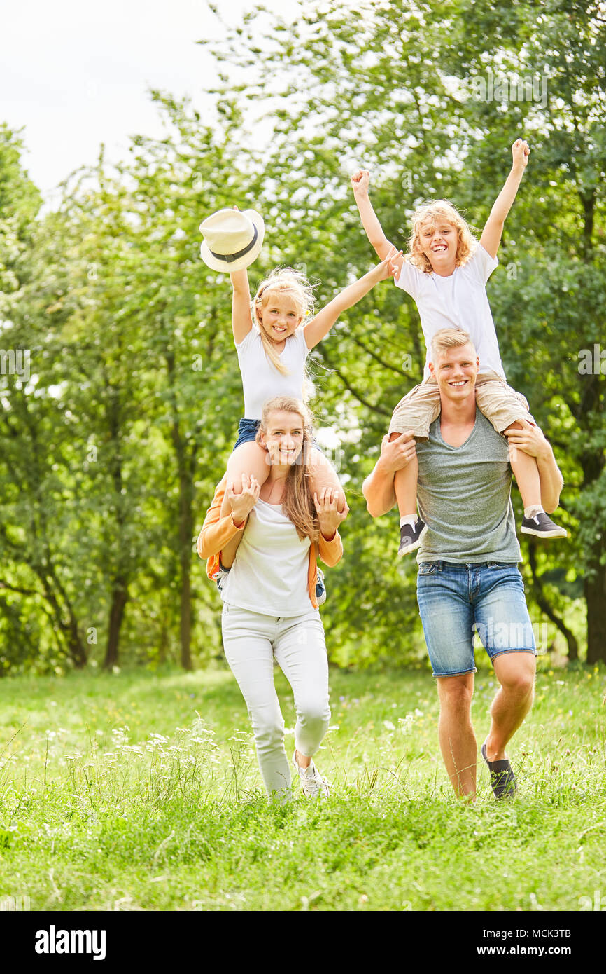 Parents carry cheerful children piggyback on a summer meadow Stock Photo