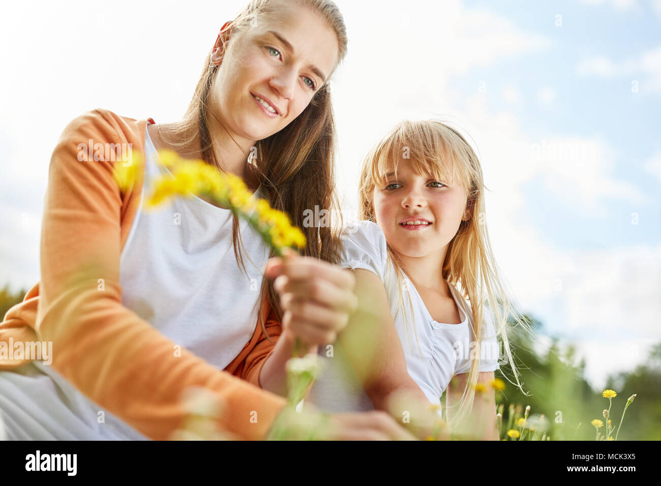 Mother and daughter tie a flower wreath from dandelion flowers Stock Photo