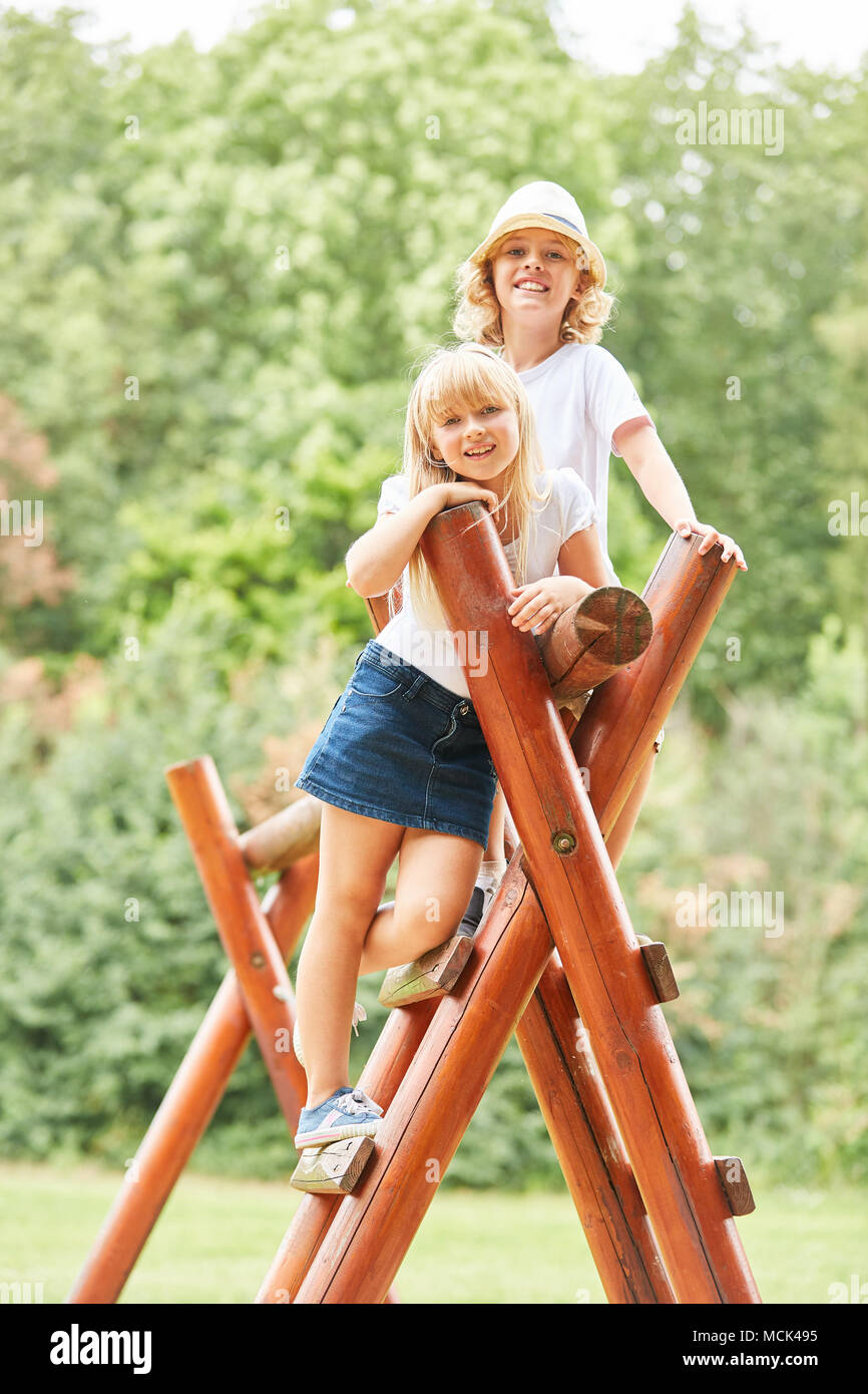 Two sibling children are smiling proudly on the climbing frame in the