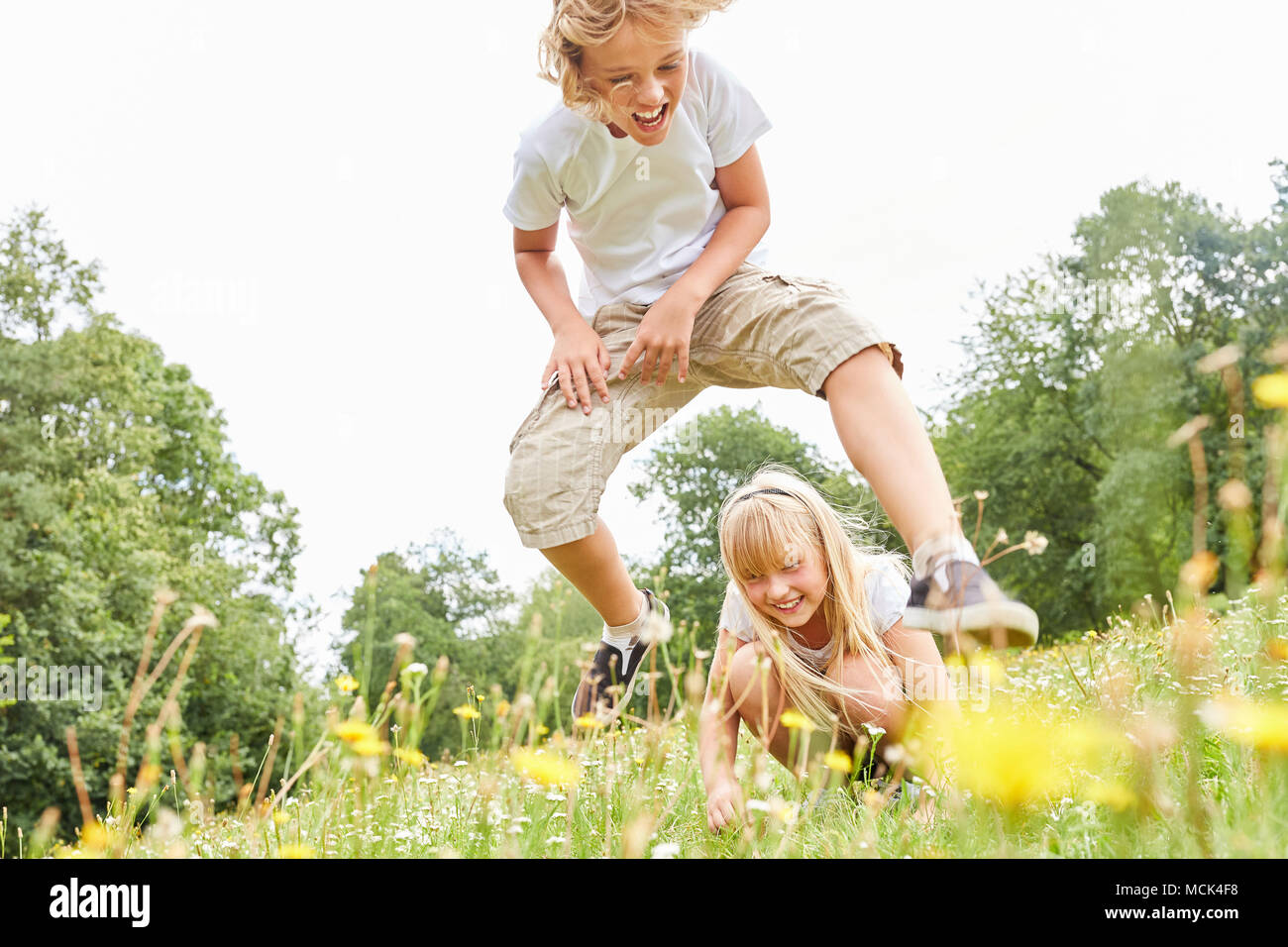 Boy in leapfrog with his sister on a meadow in summer Stock Photo