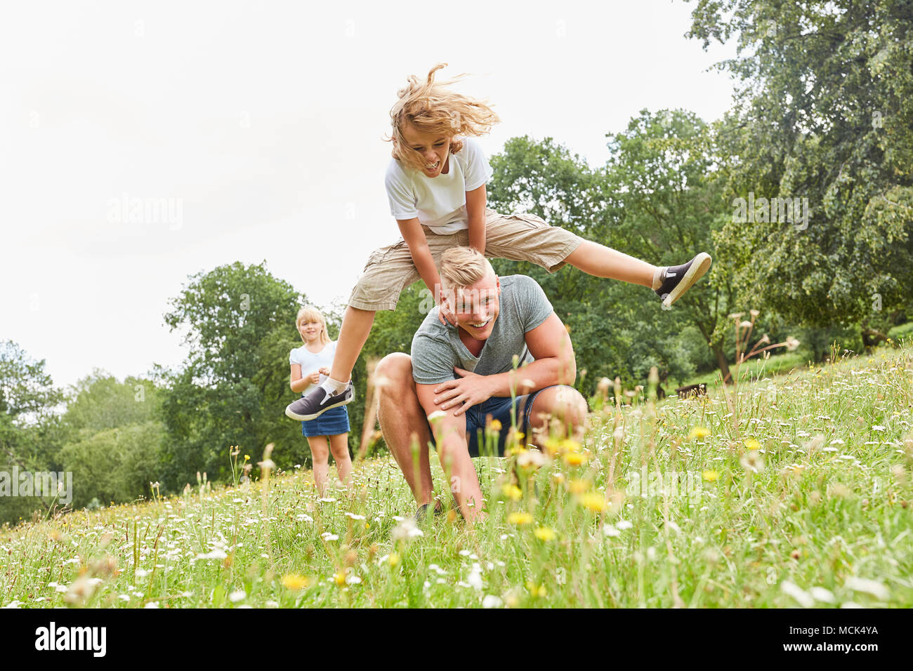 Children jumping with his dad on a meadow in summer Stock Photo