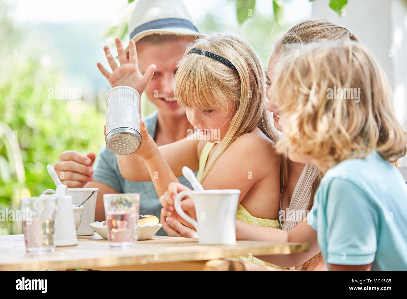 Family and girl with sugar shaker at the coffee table in the garden Stock Photo